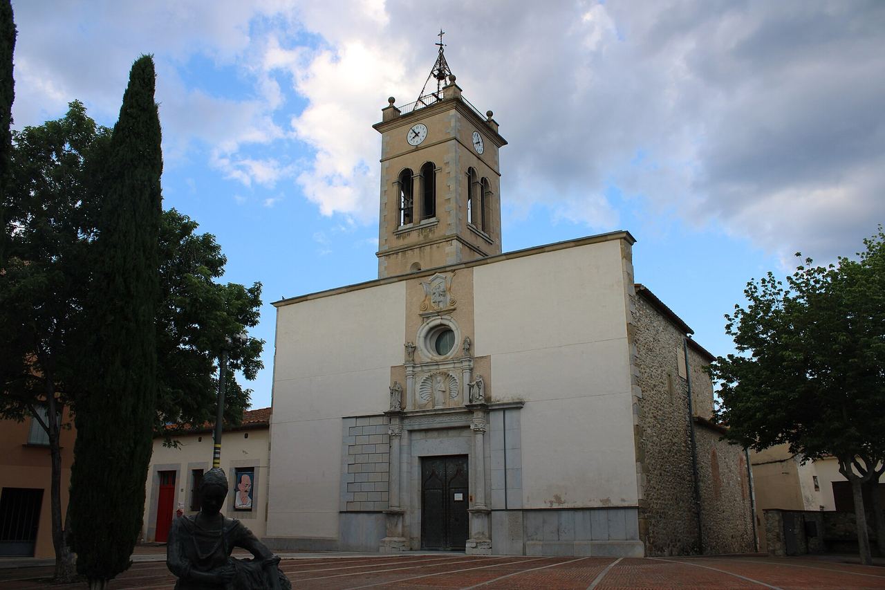 L'església de Sant Llorenç de Bescanó, amb façana blanca i rellotges al campanar; a la plaça, un xiprer i una escultura