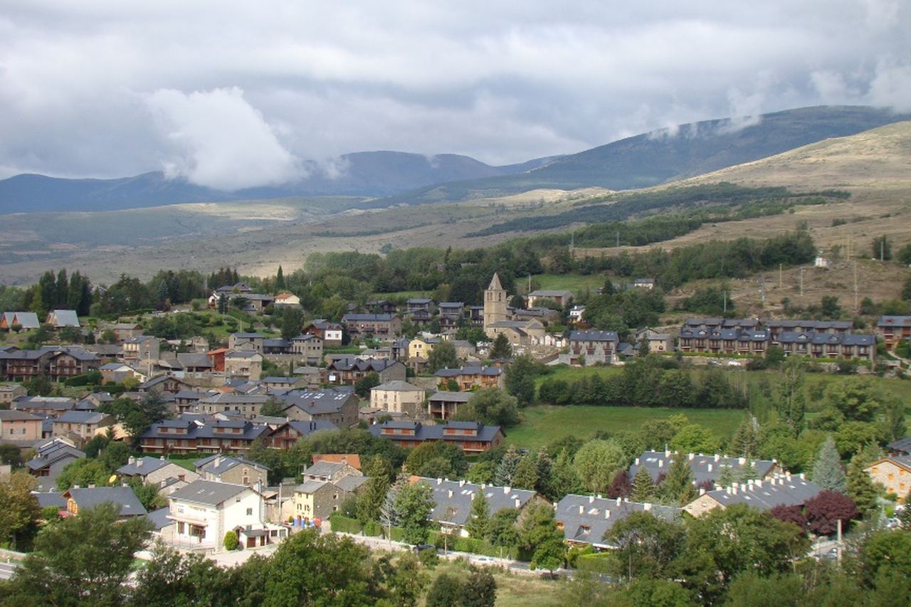 Bolvir: campanar al mig del poble, teulades de pissarra i murs de pedra entre prats i arbres, amb muntanyes i núvols baixos