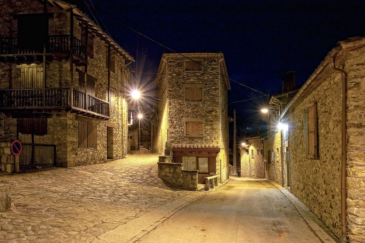 Dos carrers de Campelles de nit, il·luminats pels fanals, entre cases de pedra amb balcons de fusta i porticons