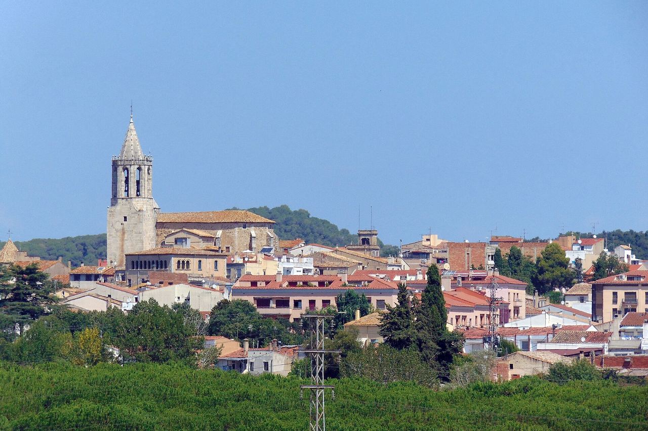 Cassà de la Selva vista de lluny: el campanar de Sant Martí sobre les teulades i turons de bosc al fons