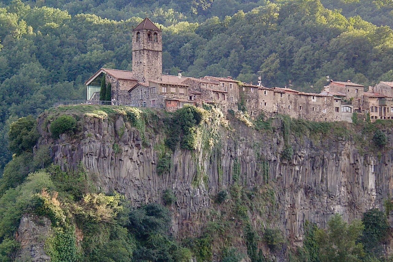 Les cases de pedra i el campanar de Castellfollit de la Roca, arrenglerats dalt d'una cinglera de roca, amb bosc al darrere
