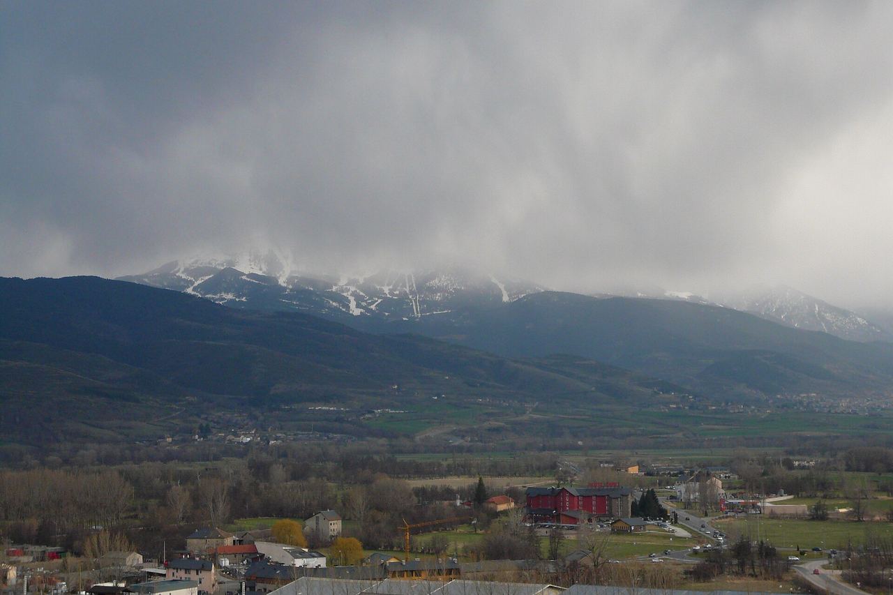 La plana de la Cerdanya un dia tapat, amb edificis de Puigcerdà en primer pla i muntanyes amb neu entre els núvols