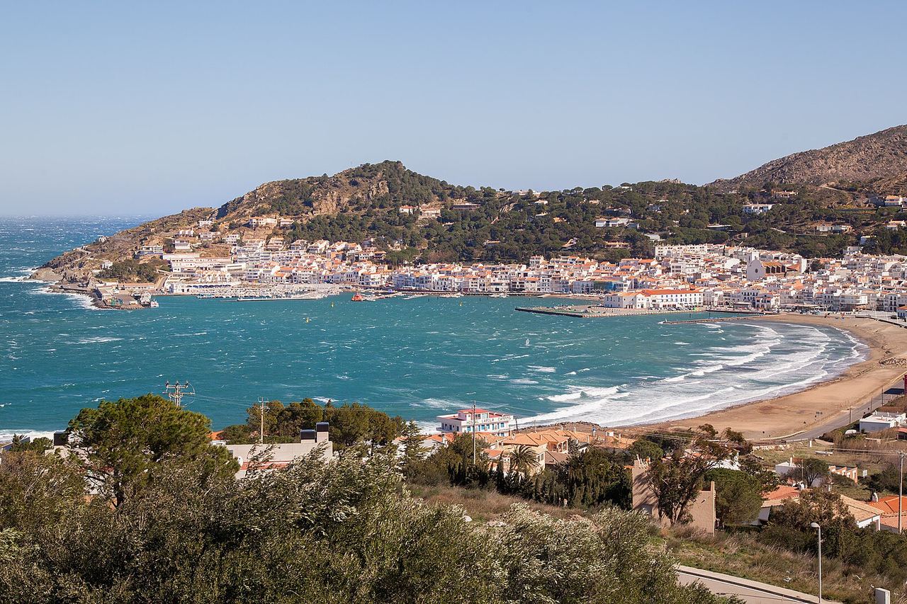 La badia del Port de la Selva, amb el poble de cases blanques, el port i la platja, i el mar picat