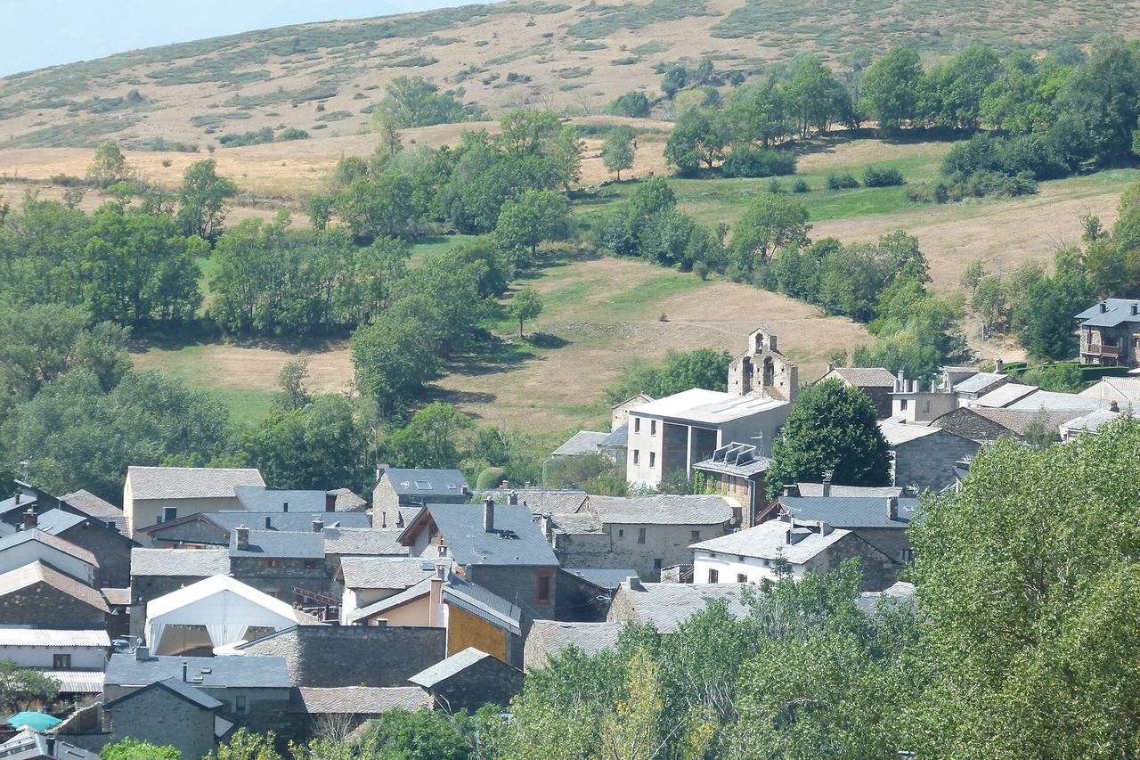 Guils de Cerdanya: cases amb teulades de pissarra entre prats verds i arbres sense fulla, amb serres nevades al fons