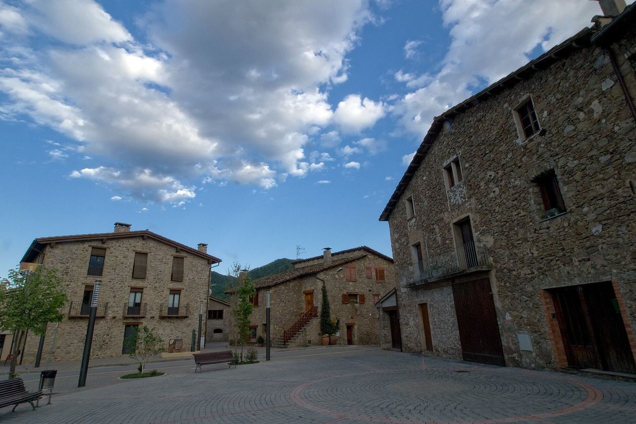 Plaça de l'Hostalnou de Bianya, a la Vall de Bianya, amb cases de pedra, una escala exterior amb barana de fusta i bancs