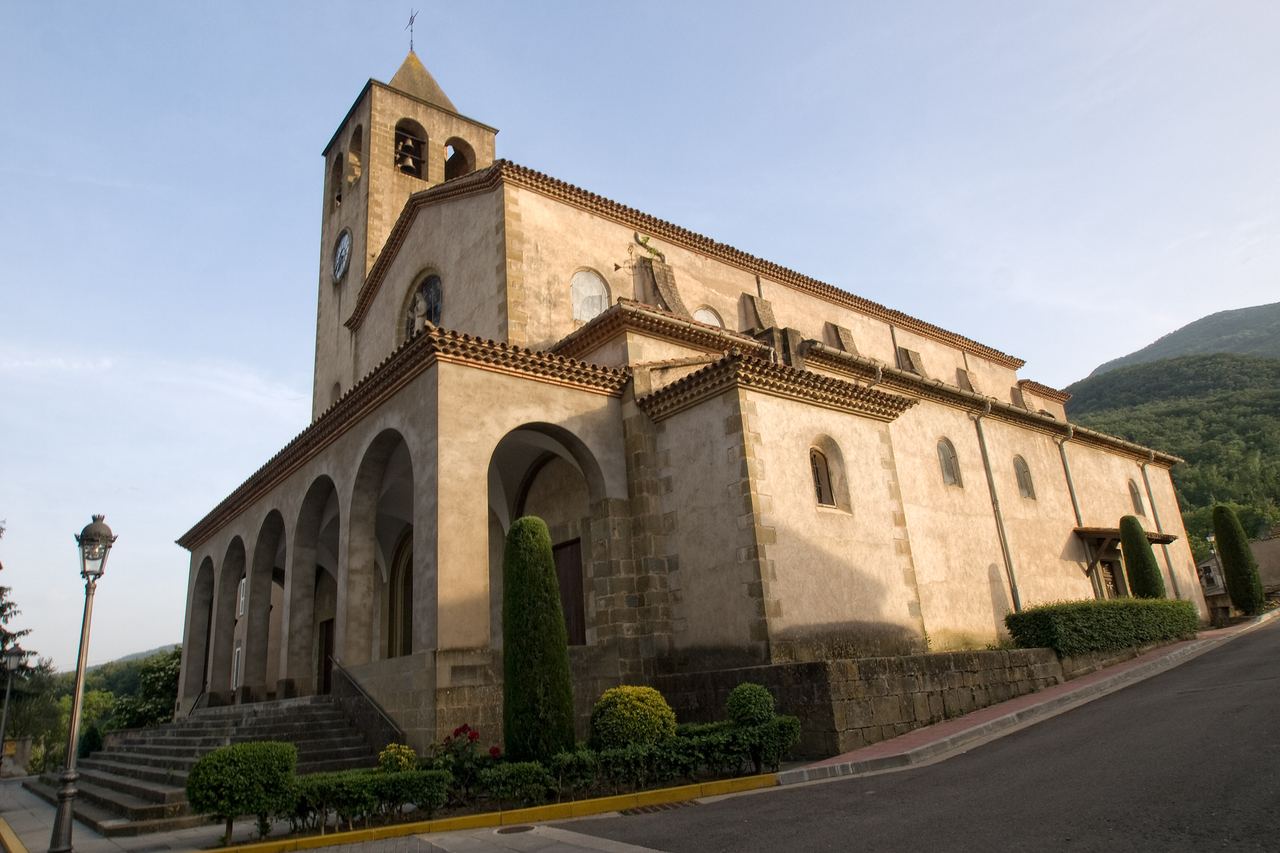 L'església de les Planes d'Hostoles, amb el campanar, un porxo d'arcs i xiprers retallats al davant