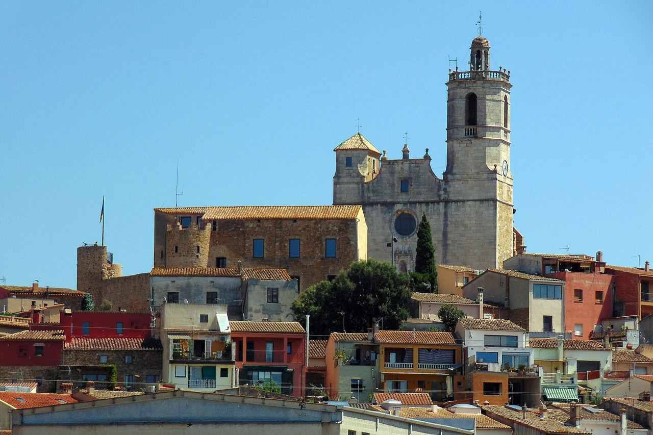 Llagostera dalt del turó, amb l'església de Sant Feliu, una torre de pedra amb bandera i cases de colors al vessant