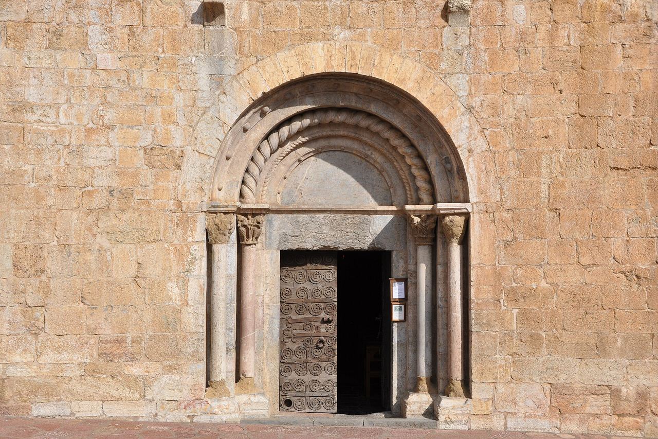 Campanar de pedra de l'església de Llanars, amb teulada piramidal i finestres d'arc, i un xiprer sota el cel blau