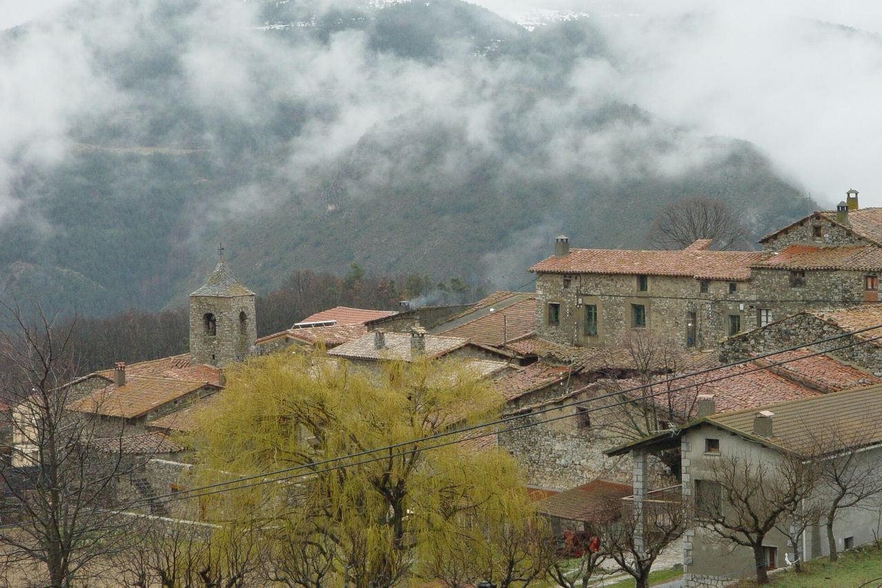 Travesseres, a Lles de Cerdanya: cases de pedra i teula, un campanar i la muntanya del darrere mig amagada per la boira