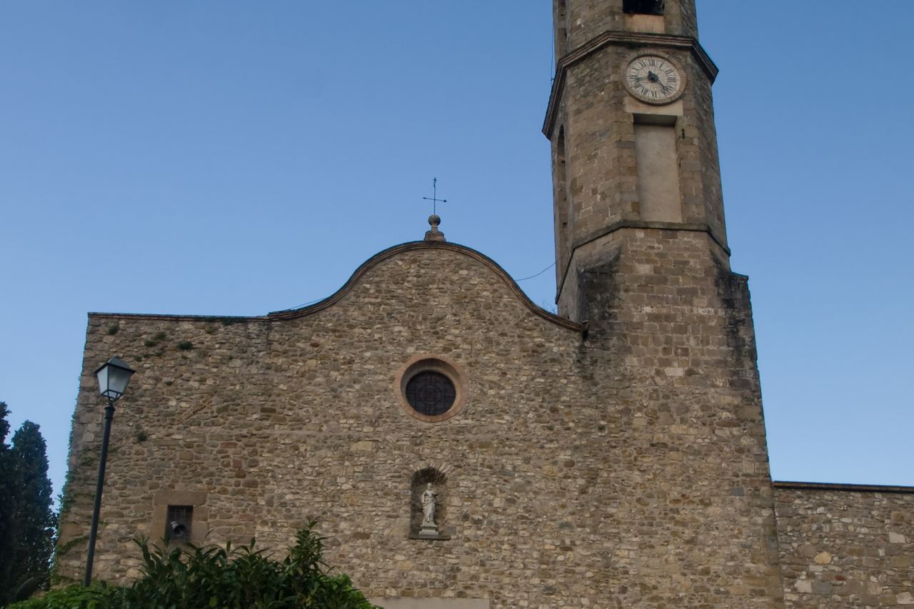 Façana de pedra de l'església de Mieres, amb un òcul, una imatge en una fornícula i el rellotge al campanar