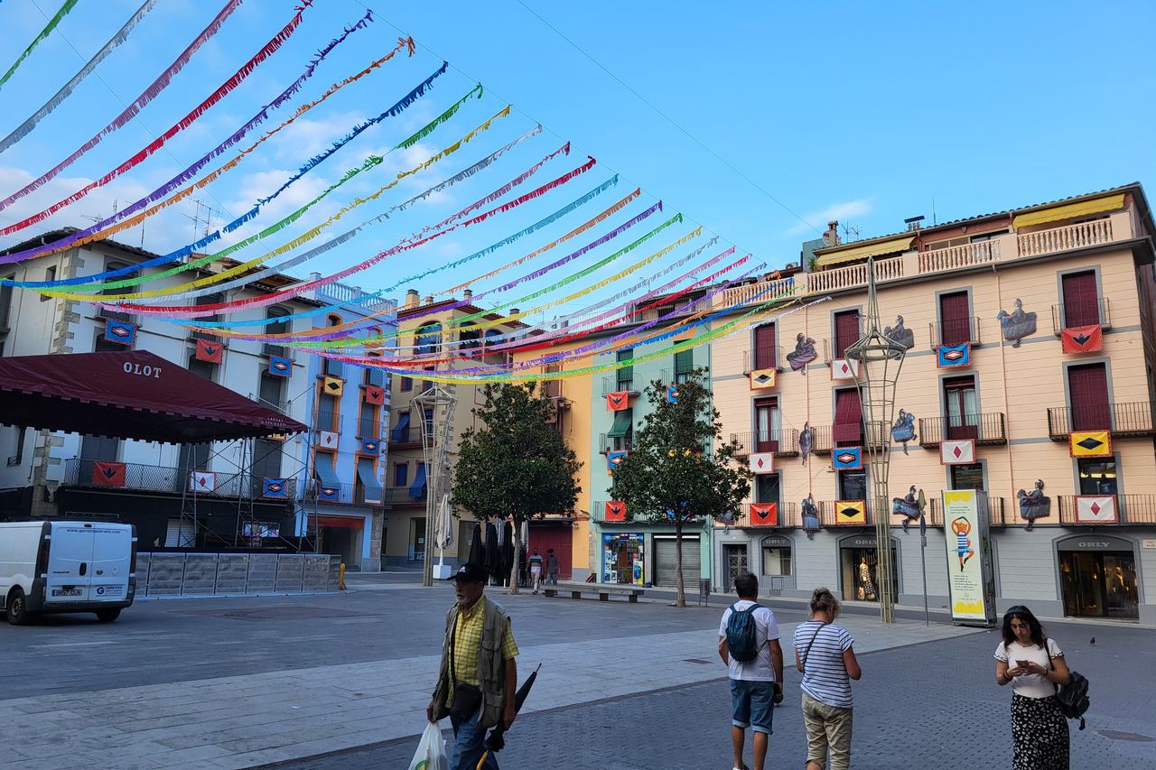 La plaça Major d'Olot guarnida amb garlandes per la festa major, amb gent passejant