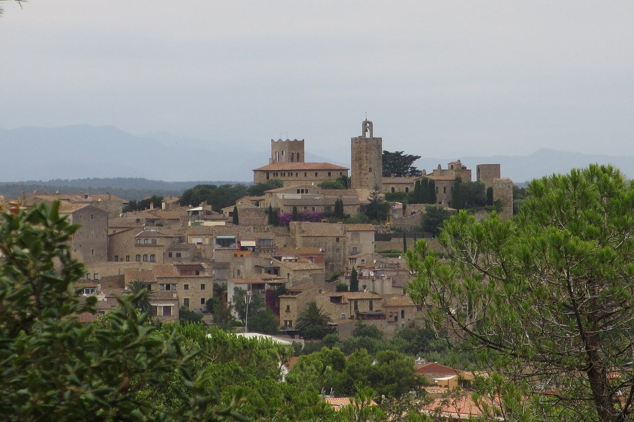 Les cases de pedra de Pals pugen fins a les torres, entre xiprers, amb un pi en primer terme i muntanyes amb boira al fons
