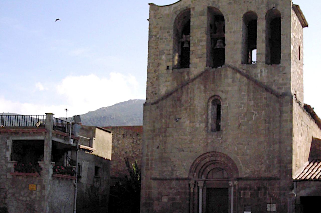 L'església de Pau, de pedra, amb la portalada d'arcs i el campanar, i cases amb balcons florits al costat
