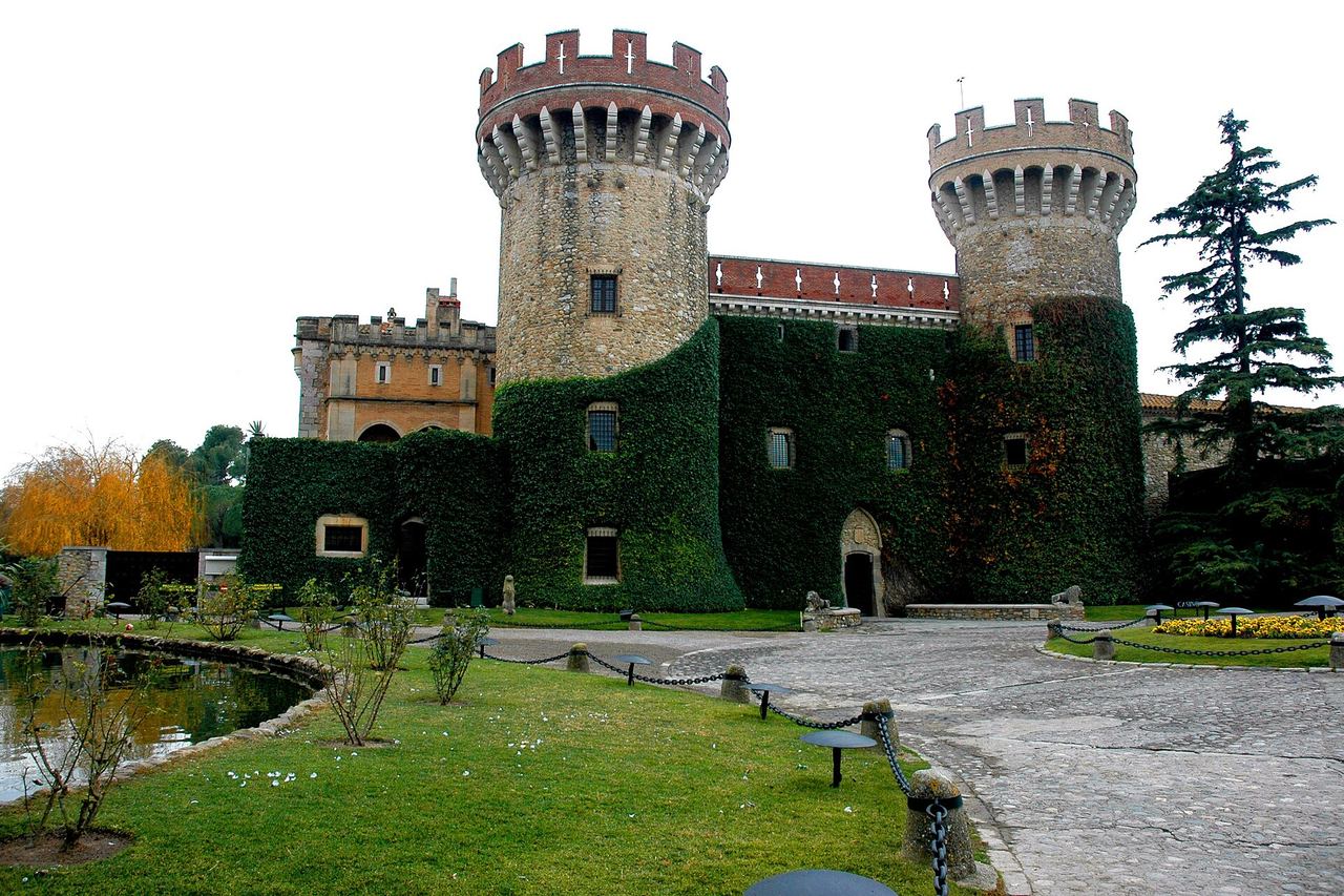 El castell de Peralada, amb dues torres rodones emmerletades i la façana coberta d'heura, davant d'un pati empedrat