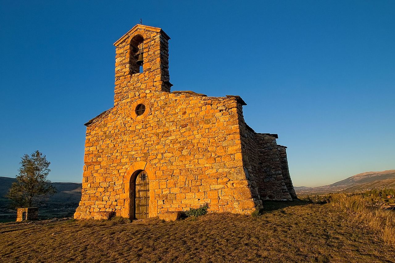 Església de pedra amb un petit campanar d'una campana, daurada pel sol dalt d'un turó de Prats i Sansor, amb la vall al fons