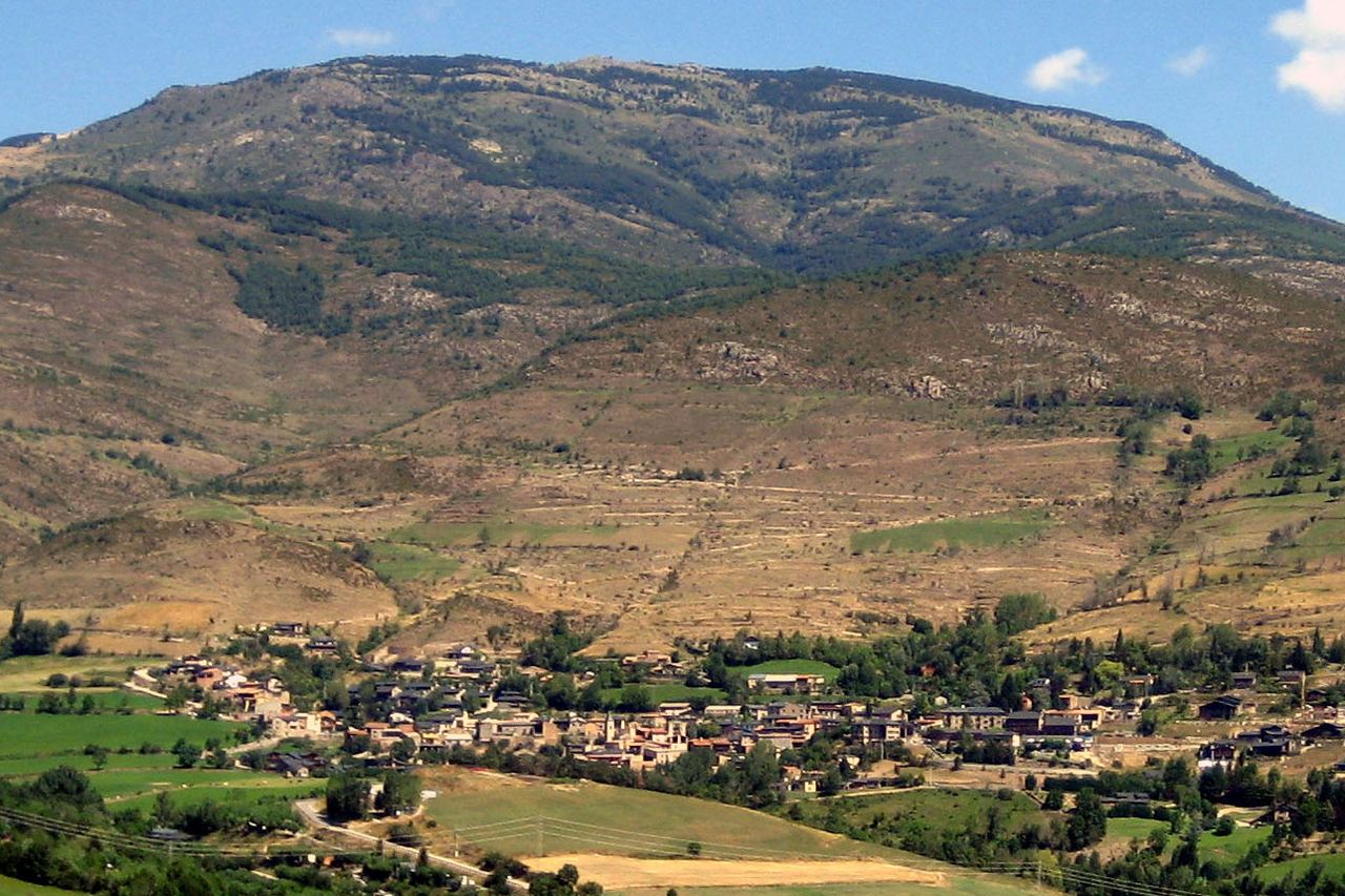 Prullans vist de lluny: les cases del poble entre prats i arbres, als peus d'una muntanya amb feixes