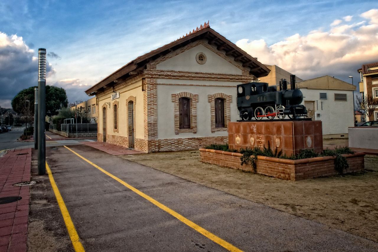 L'estació del carrilet de Quart, amb el rètol del poble a la façana i una locomotora de vapor negra sobre un pedestal