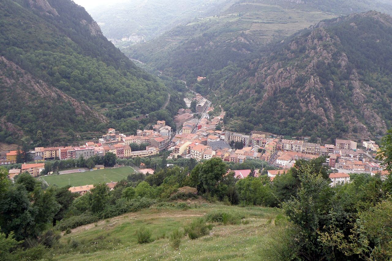 Ribes de Freser vist des de dalt, al fons d'una vall estreta entre muntanyes de bosc i roca, amb un camp de futbol