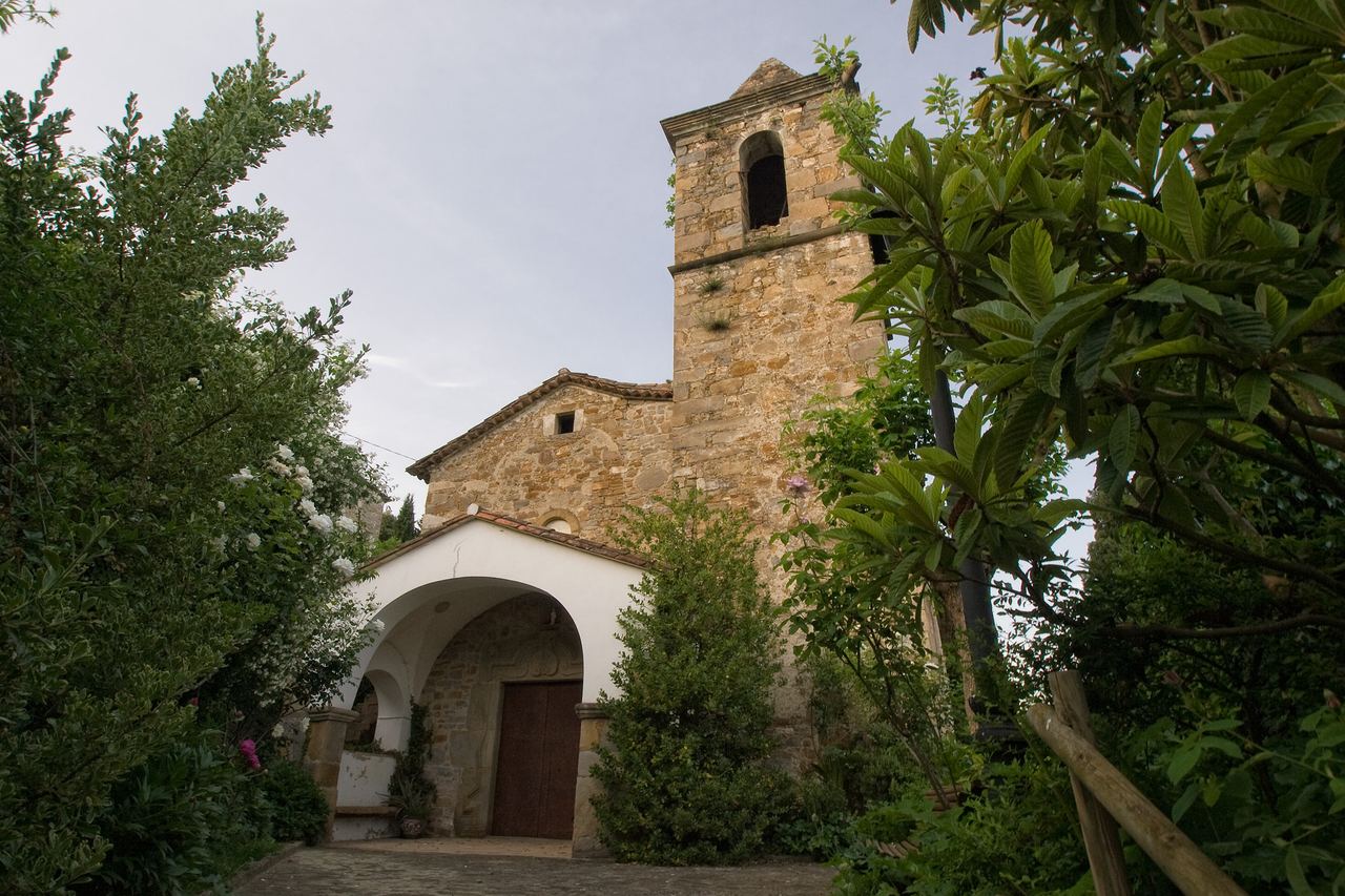 L'església de pedra de Sant Aniol de Finestres, amb el campanar i un porxo blanc amb arc, entre la vegetació