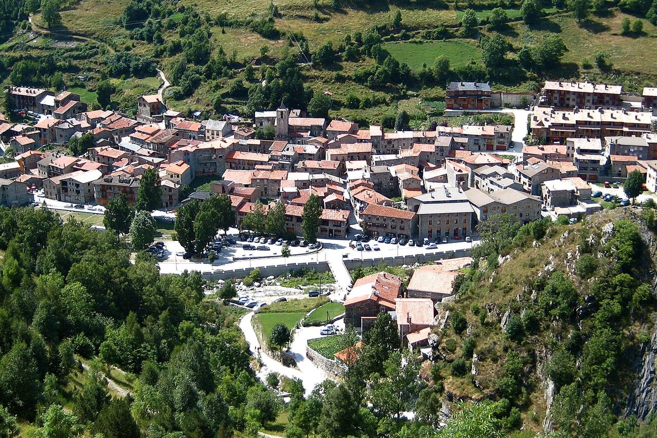 Setcases vist des de dalt: cases de pedra amb teulades vermelles al voltant del campanar, entre prats i boscos de muntanya