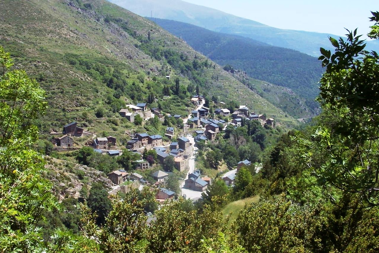 Les cases de pedra de Toses escampades pel vessant d'una vall, vistes entre arbres, amb serres al fons