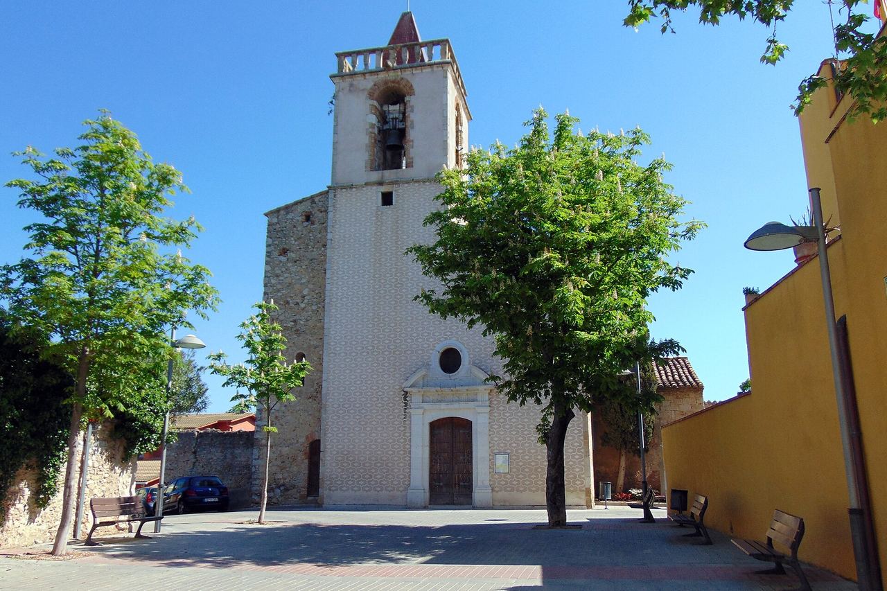 L'església de Sant Cebrià de Vilafant, amb el campanar i la façana decorada amb un motiu geomètric; al davant, arbres i bancs